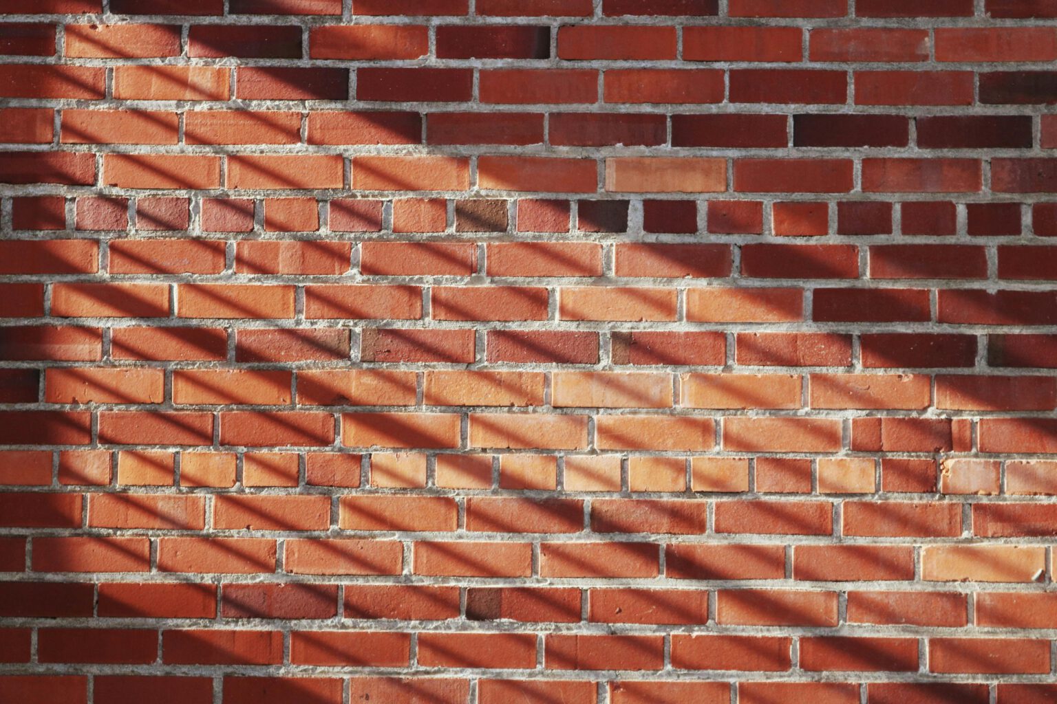 Red brick wall with striking shadows creating a textured pattern.