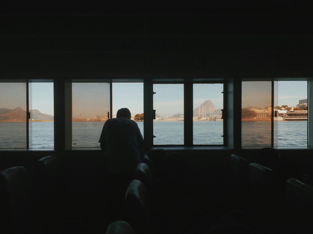 A silhouette of a man on a boat gazing at Rio de Janeiro's skyline through windows, capturing the sunset glow over the sea.
