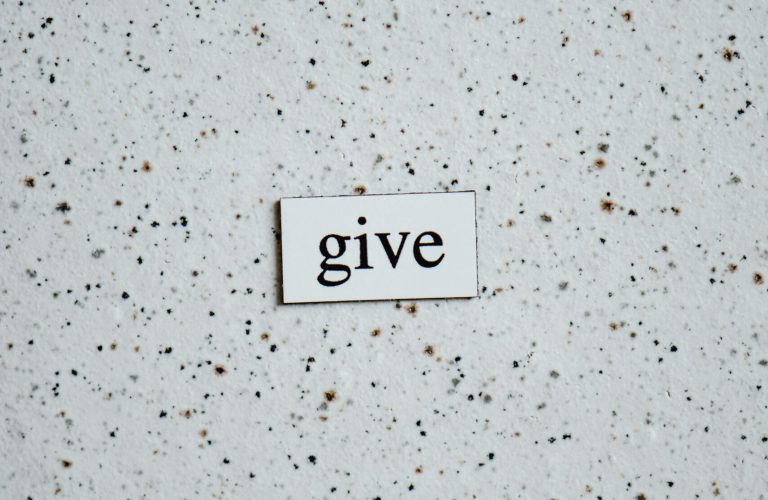 High-angle photo of the word 'give' on a speckled surface, emphasizing simplicity and minimalism.